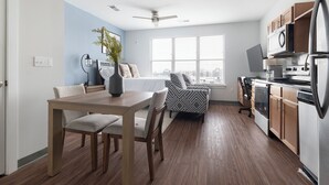 A modern kitchen with a dining area, wooden flooring, and a large window providing natural light. - Landing Apartments near Five Points South (Birmingham)