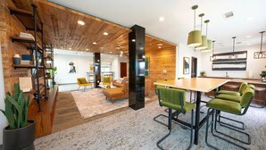 A modern interior with a wooden ceiling, a central dining area with green upholstered chairs, and a visible kitchen area. - Landing Apartments near Five Points South (Birmingham)