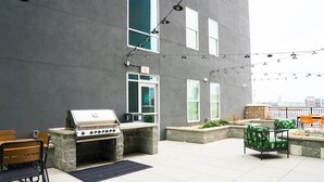 An outdoor patio with a stone barbecue grill, seating area, and string lights. - Landing Apartments near Five Points South (Birmingham)