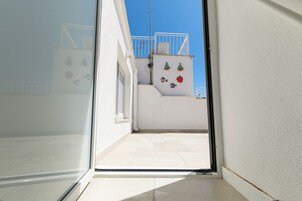 A narrow corridor leading to a balcony with a white railing and a small window.