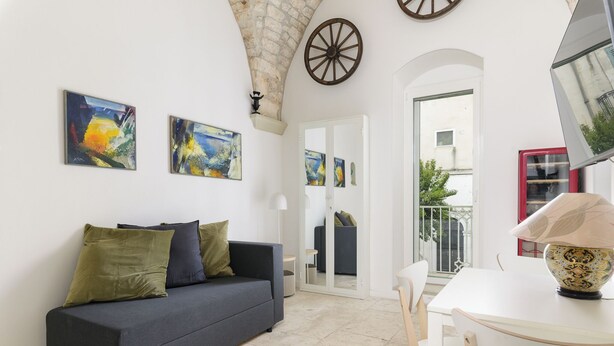 A living room with a dark sofa, a white table, and artwork on the walls. There is a door leading to another room and a balcony with a railing. - Casa F&G with Terrace by Wonderful Italy (Ostuni)