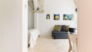 A room with a bed, a sofa, and a small table. There are two paintings on the wall and a stone archway. - Casa F&G with Terrace by Wonderful Italy (Ostuni)