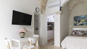 A bedroom with a bed, a TV, a desk with chairs, and a kitchen area in the background. - Casa F&G with Terrace by Wonderful Italy (Ostuni)