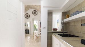 A modern kitchen with a stone backsplash, a stainless steel sink, and a dining area with a white table and chairs. - Casa F&G with Terrace by Wonderful Italy (Ostuni)
