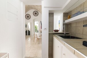 A modern kitchen with a stone backsplash, a stainless steel sink, and a dining area with a white table and chairs.