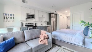 Un apartament modern amb una cuineta, un sofà gris, un llit i una planta en test.