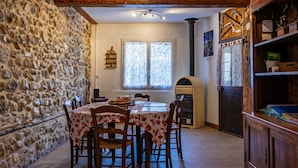 A rustic dining area with a stone wall, wooden beams, a table with chairs, a fireplace, and a wooden cabinet. - House in a Hamlet in the Heart of Cathar Country (Quillan)