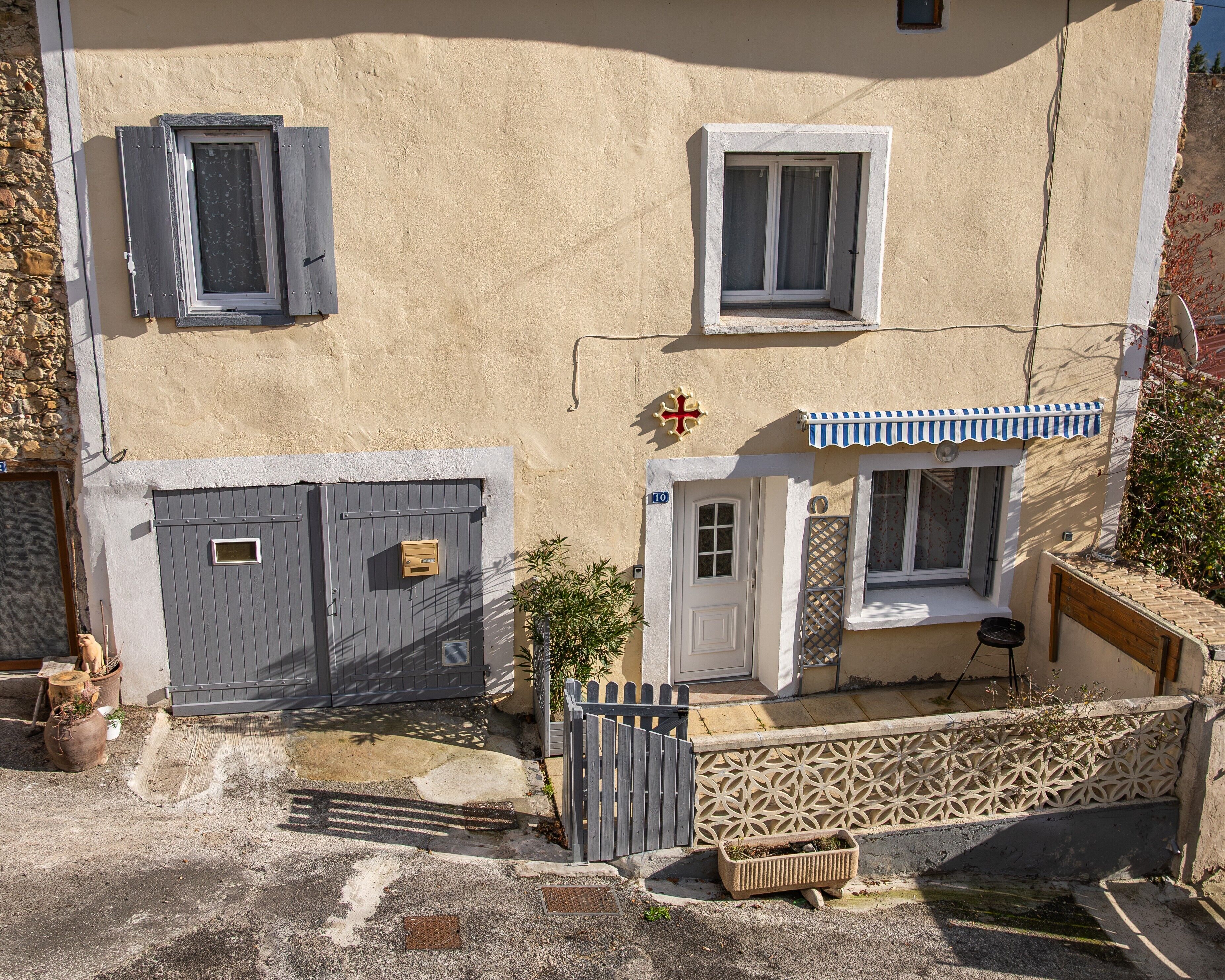 A two-story building with a grey door, a small window with a white frame, and a balcony with a blue and white awning.