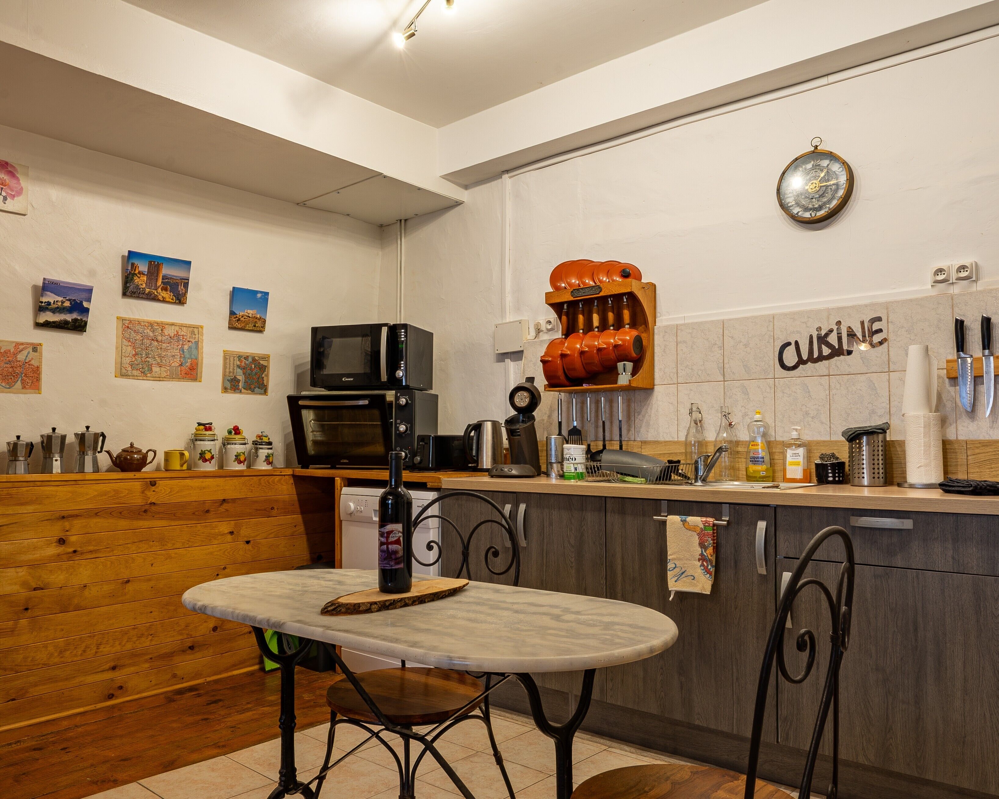 Een keuken met een houten bankje, een tafel, een magnetron, een koffieapparaat en een fles wijn.
