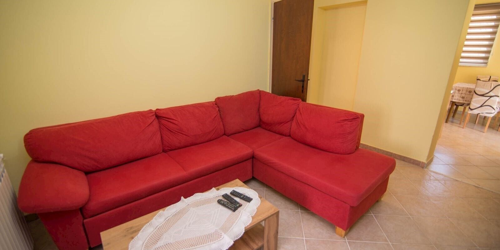 A red sectional sofa in a room with a tiled floor and a wooden coffee table with remote controls.