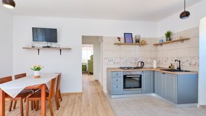 A modern kitchen with a dining area, built-in oven, and a TV mounted on the wall. - Pino 1 in Veli Lošinj (Veli Lošinj)