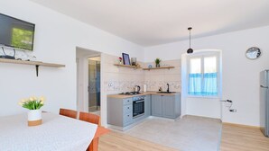 A modern kitchen with grey cabinets, a wooden countertop, and a built-in oven. There is a dining table with a vase of flowers and a TV mounted on the wall. - Pino 1 in Veli Lošinj (Veli Lošinj)