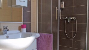 Un bagno con un lavandino bianco, uno specchio, un asciugamano viola e una doccia con soffione manuale.