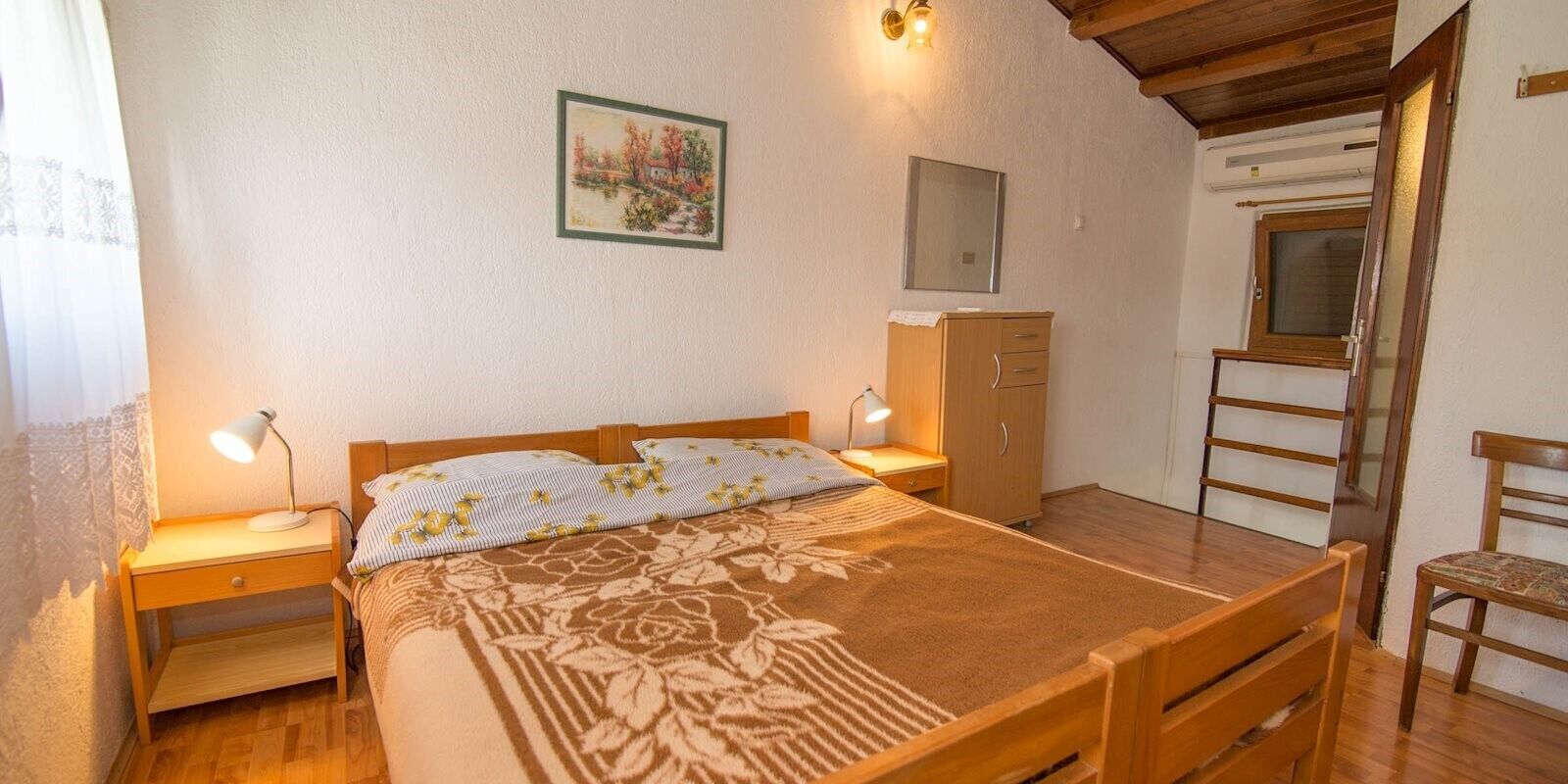 Ein Schlafzimmer mit einem Bett, Nachttischlampen, einem Holzschrank, einem Stuhl und einem Gemälde an der Wand.