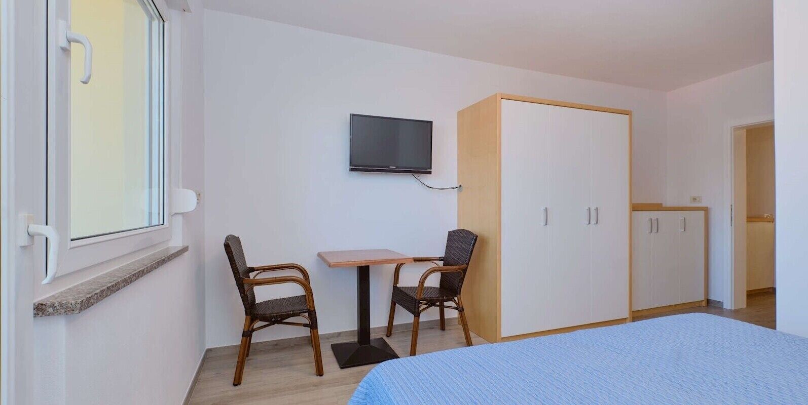 Une chambre à coucher comprenant un lit, un téléviseur fixé au mur, une armoire et deux chaises.