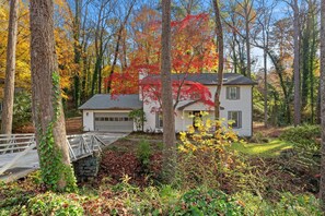 A white house with a garage, surrounded by autumn foliage and a stone wall. - 5BR Smyrna Home Near the Battery (Smyrna)