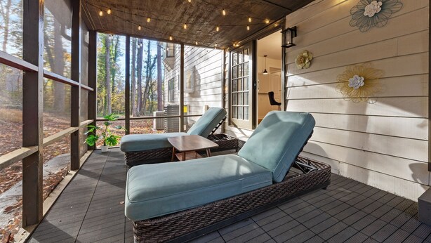 A covered outdoor seating area with wicker furniture, large windows, and decorative wall art. - 5BR Smyrna Home Near the Battery (Smyrna)