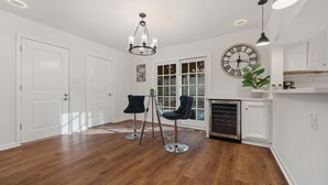 A spacious room with hardwood flooring, a chandelier, two bar stools, a large window with a view, and a clock on the wall. - 5BR Smyrna Home Near the Battery (Smyrna)