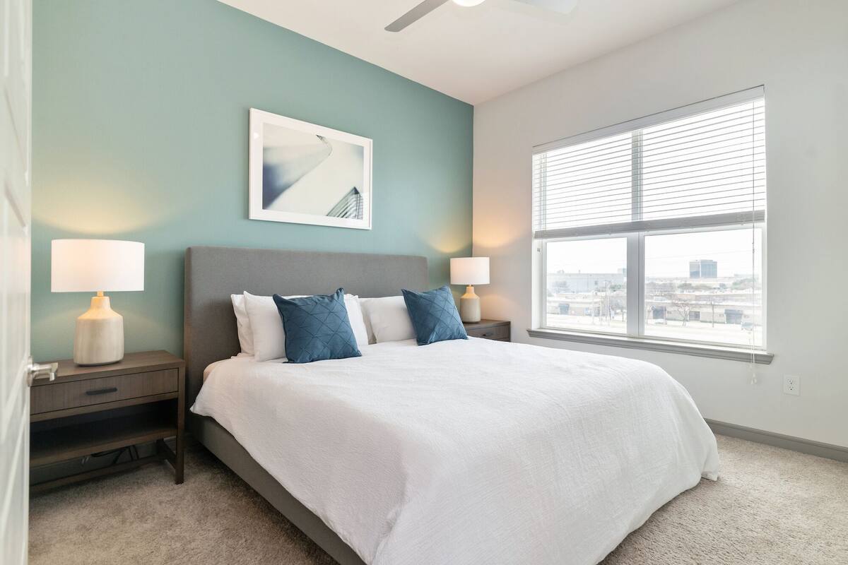 A bedroom with a bed, two bedside tables, a window with blinds, and a ceiling fan.