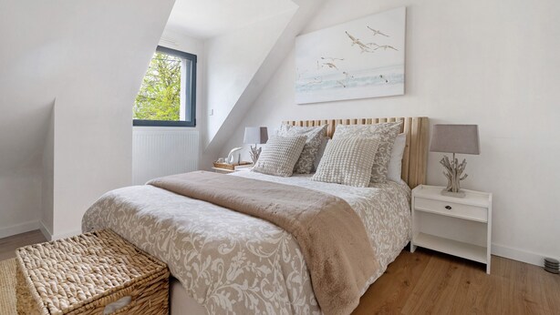 A bedroom with a sloped ceiling, a bed with patterned bedding, a nightstand with a lamp, and a painting of birds.