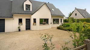 A two-story house with a gravel driveway, a black door, and a small garden with potted plants.