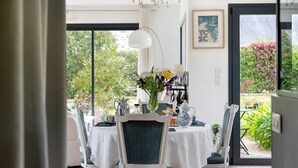 A dining area with a table set for four, chairs with blue cushions, a vase with flowers, and a view of greenery outside.