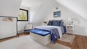 Ein Schlafzimmer mit schrägem Dach, einem Bett mit blauer Bettwäsche, einem weißen Heizkörper, einem Stuhl und einem Fenster.