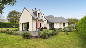 Ein modernes, zweistöckiges Haus mit überdachter Terrasse, kleinem Garten und einem sichtbaren Schornstein.