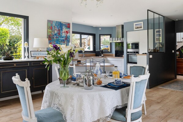 Comedor con mesa dispuesta para el desayuno, cocina al fondo y vistas al exterior.