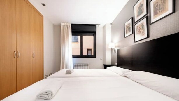 Een hotelkamer met twee bedden, een houten garderobe, een raam met uitzicht en ingelijste foto's aan de muur.
