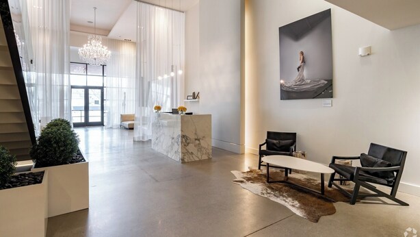 En rymlig lobby med en marmordiskin reception, moderna stolar, en kristallkrona och ett stort inramat konstverk på väggen.