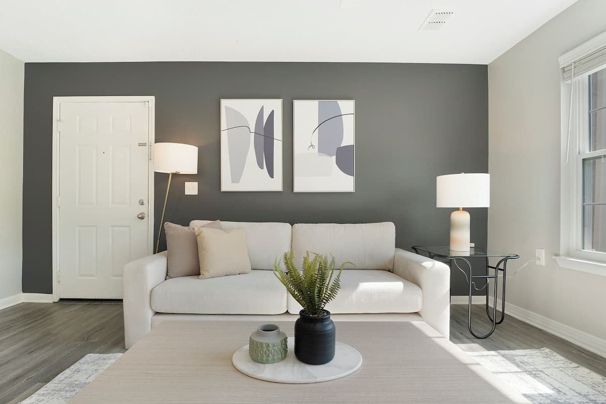 A modern living room with a grey accent wall, a white sofa, two floor lamps, and a potted plant.