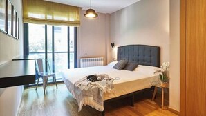 Un dormitorio moderno con una cama grande, una silla, una mesita y una ventana con cortinas.