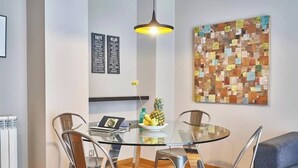 Un comedor moderno con una mesa de vidrio, sillas de metal, una lámpara colgante y una obra de arte colorida en la pared.