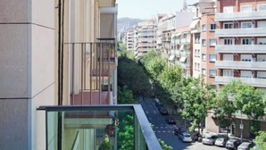 Un edificio residencial de diseño moderno, con balcones de barandilla de cristal y vista a una calle arbolada.