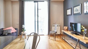 Una sala de estar moderna con un sofá, una mesa de centro, un televisor sobre un mueble de madera y un ventanal con cortinas.