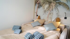 Ein Bett mit beigefarbener Bettwäsche, zwei Kissen und drei zusammengerollte Handtücher.
