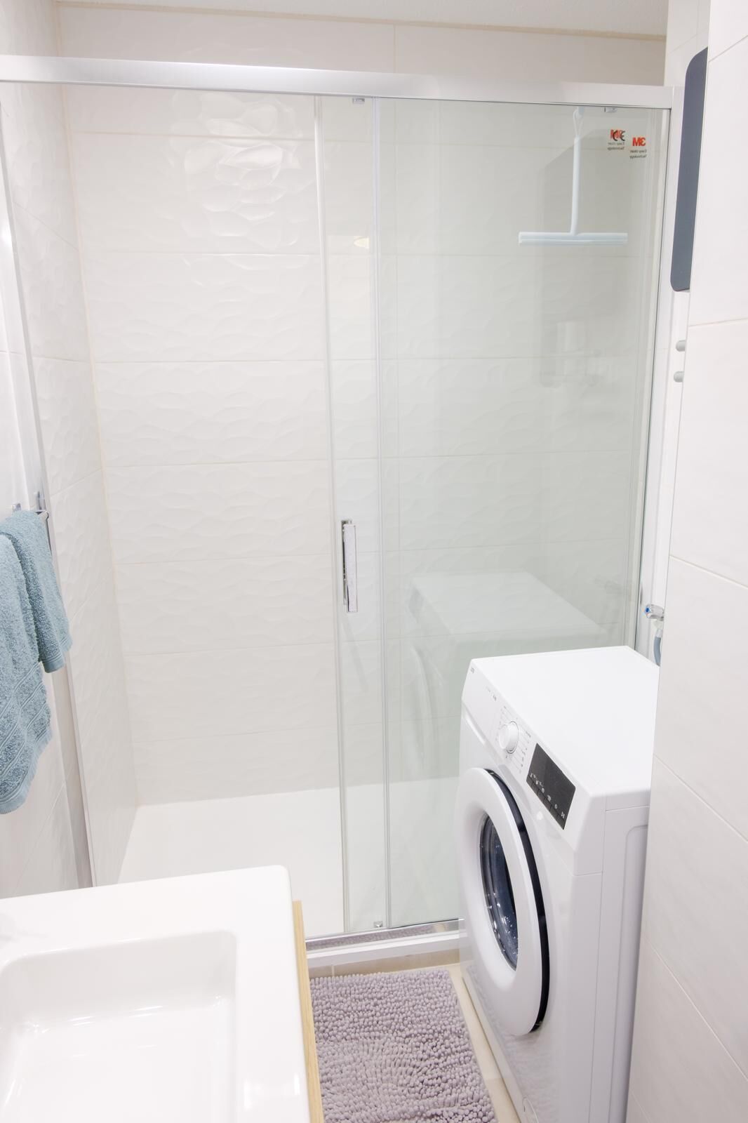 Casa de banho compacta com cabine de duche em vidro, máquina de lavar roupa e lavatório branco.