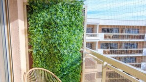 Ein Balkon mit zwei Korbstühlen, einem Tisch mit Glasplatte und einem vertikalen, grünen Garten.