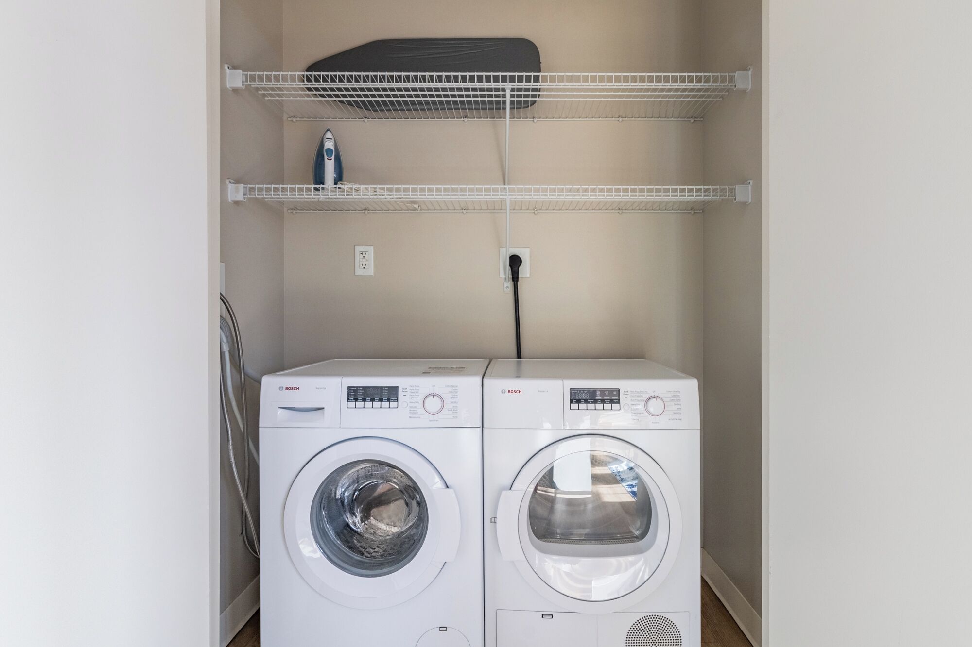 A laundry area with two white Bosch washing machines and a drying rack above them.