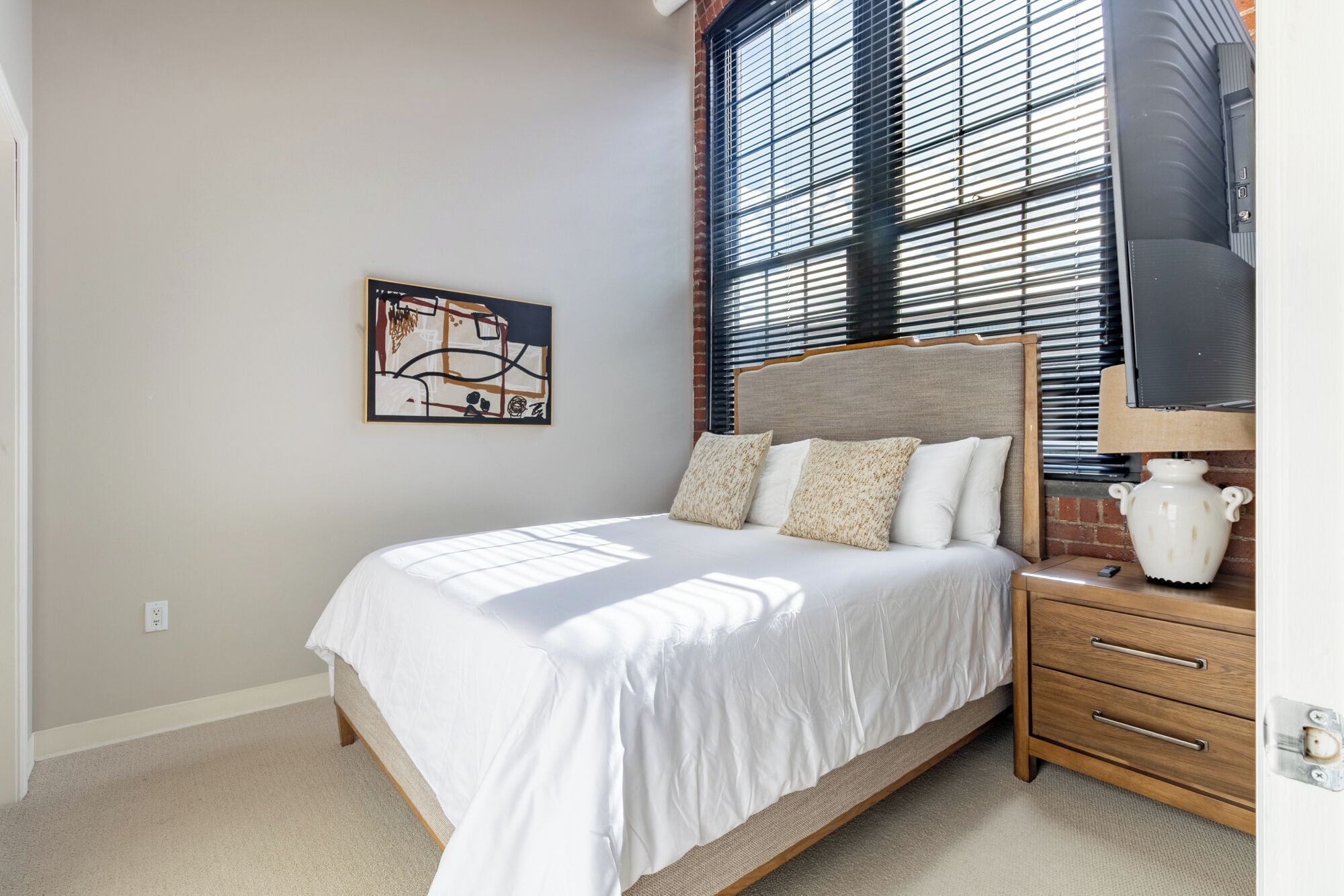 A bedroom with a bed, a nightstand, a lamp, and a wall-mounted TV.