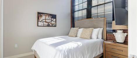 A bedroom with a bed, a nightstand, a lamp, and a wall-mounted TV.