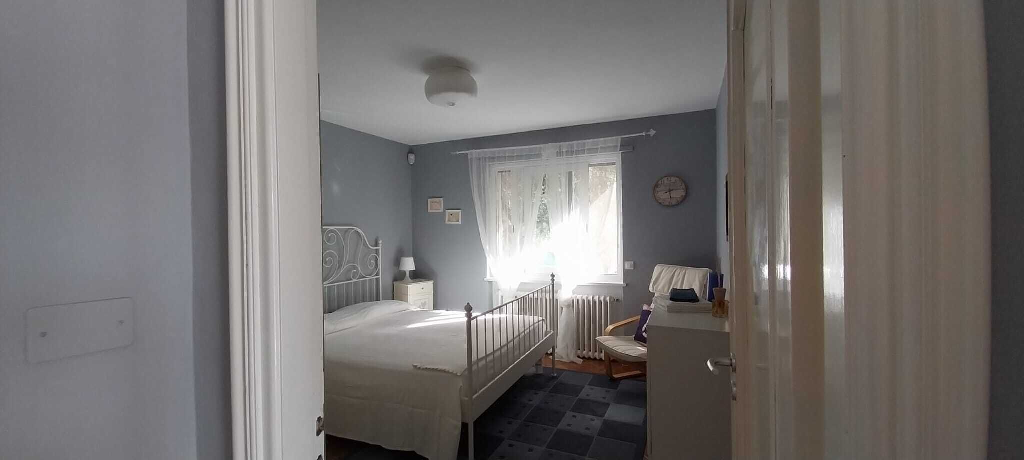 A bedroom with a bed, bedside table, lamp, and a window with curtains.
