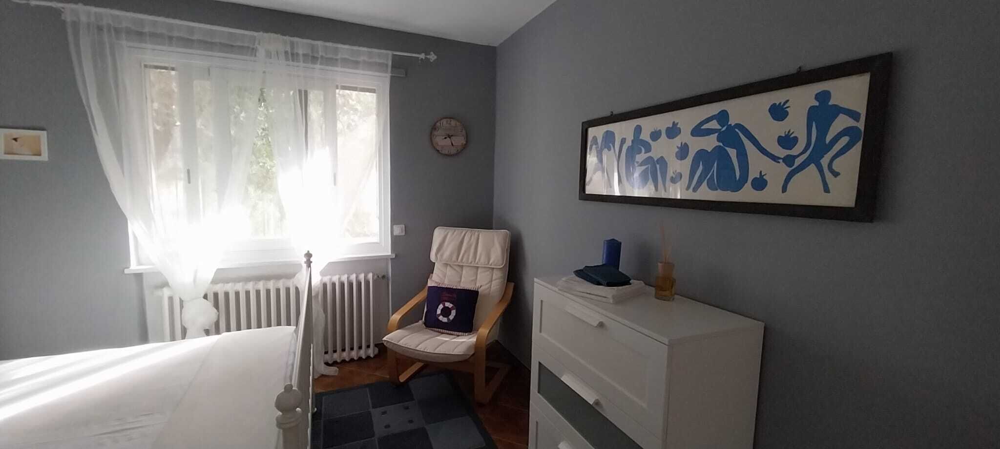 A bedroom with a bed, a chair, a dresser, a radiator, and a window with curtains.
