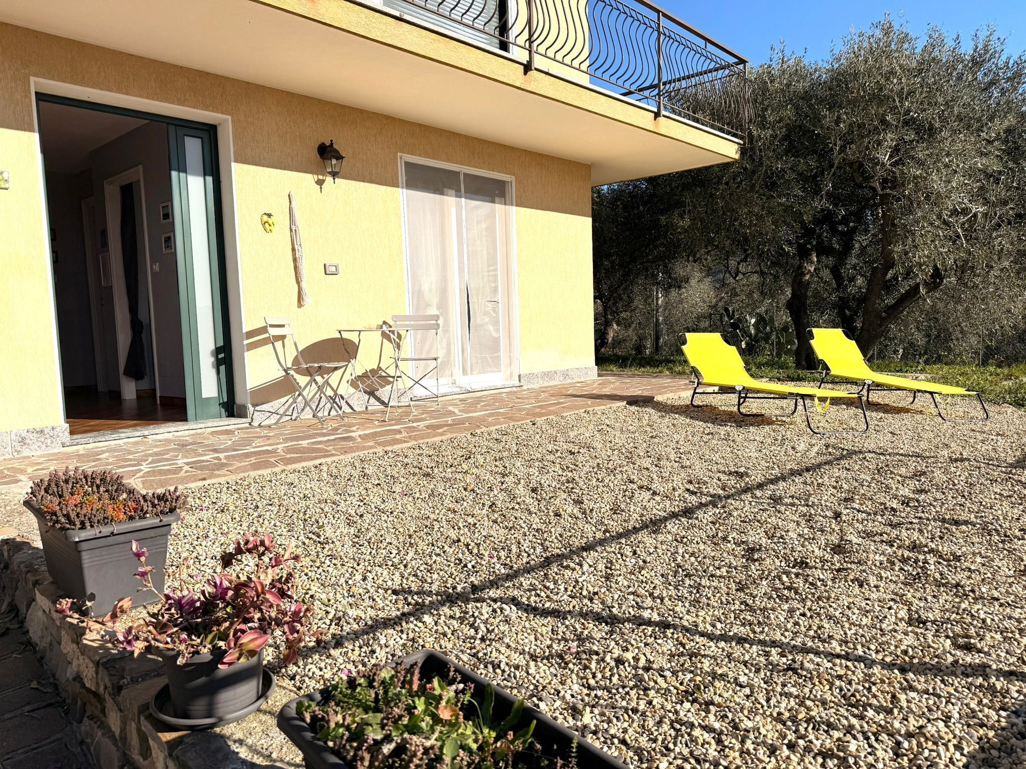 A yellow building with a balcony, outdoor seating, and potted plants.