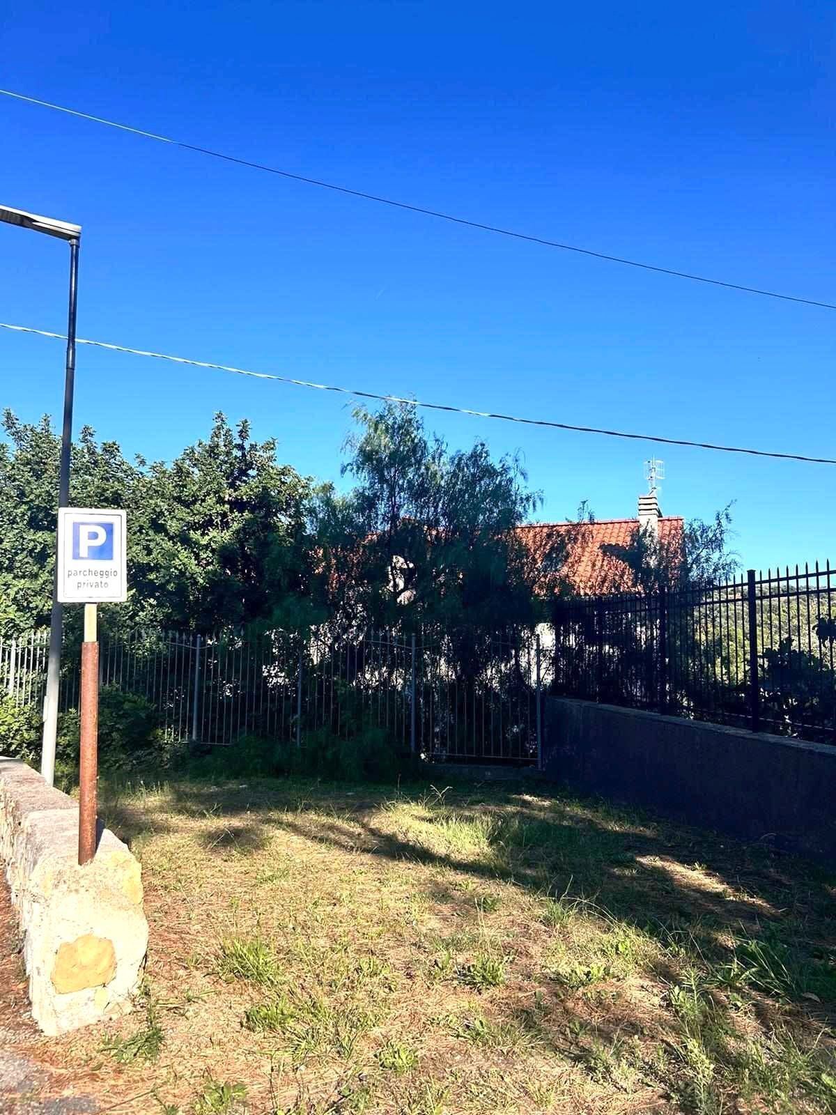 Ein Parkschild mit Privatparkplatz-Symbol, ein Metallzaun und im Hintergrund ein Gebäude mit rotem Dach.