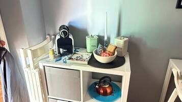 Een kleine kitchenette met een koffieapparaat, theezakjes en koffie, en een schaal met snacks.