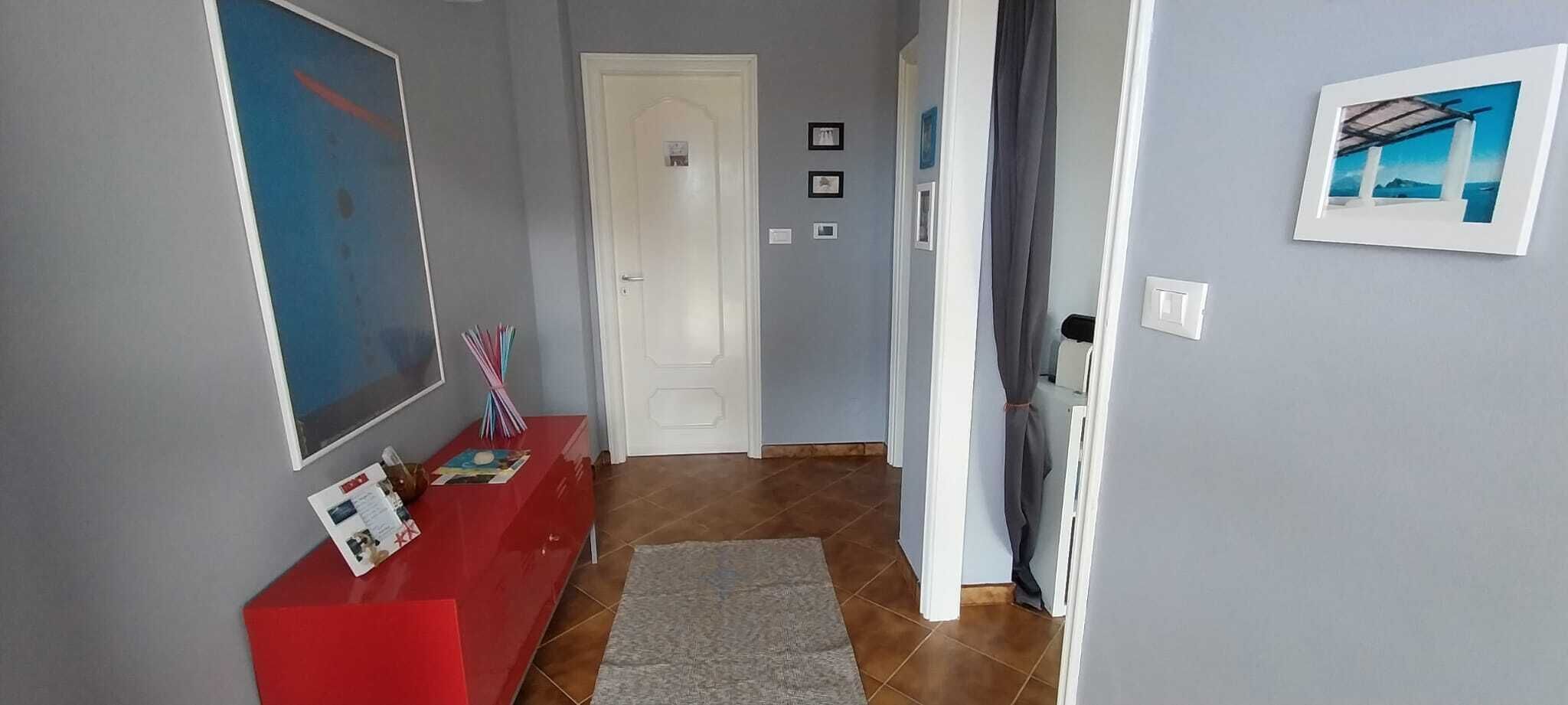A hallway with a red console table, a grey rug, and a door leading to another room.
