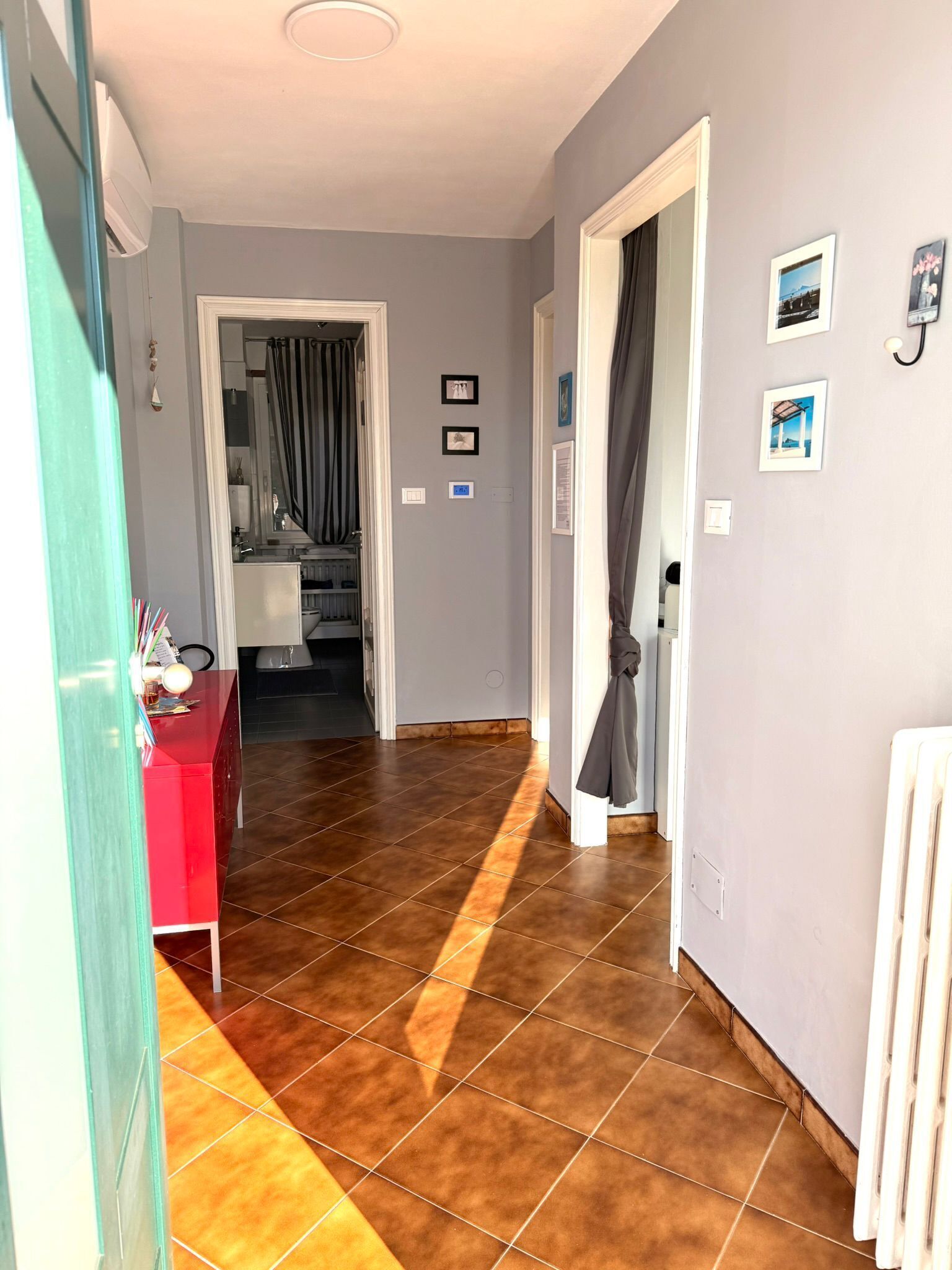 Un couloir avec un meuble rouge, un radiateur et une porte donnant sur une pièce.