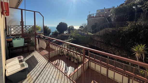 Un balcon donnant sur la mer, un mur en pierre et un escalier menant à un bâtiment.